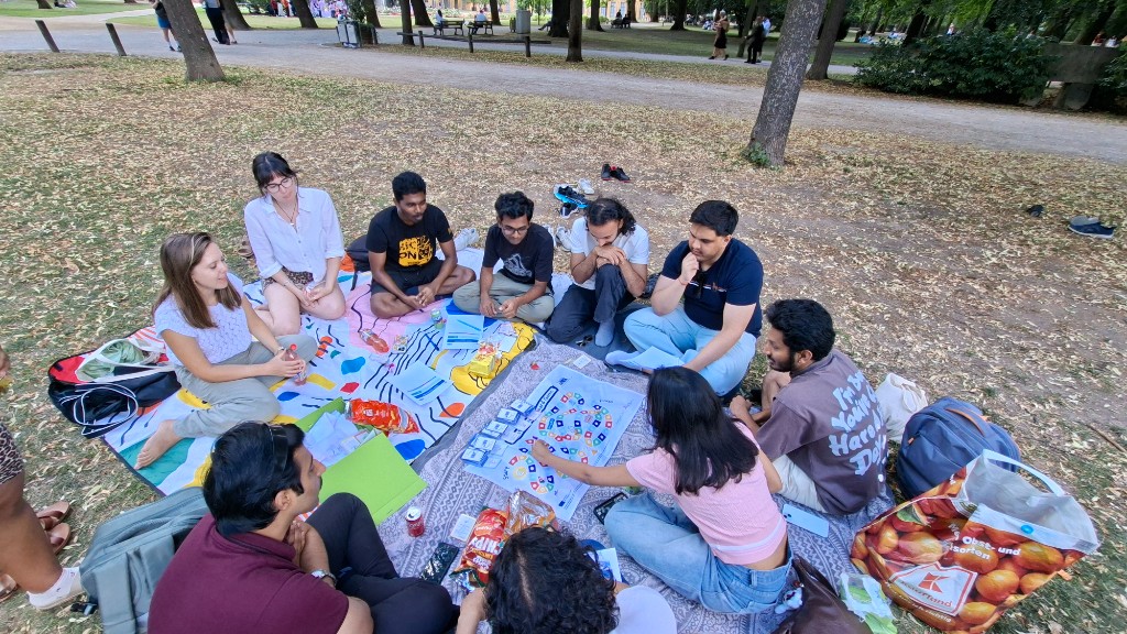 Young adults sitting in a circle on blankets in a park, playing a board game together