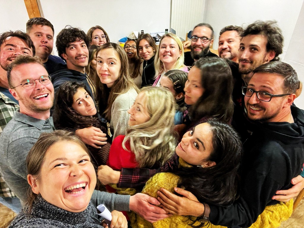A diverse group of young adults gathered in a close circle, smiling up at the camera